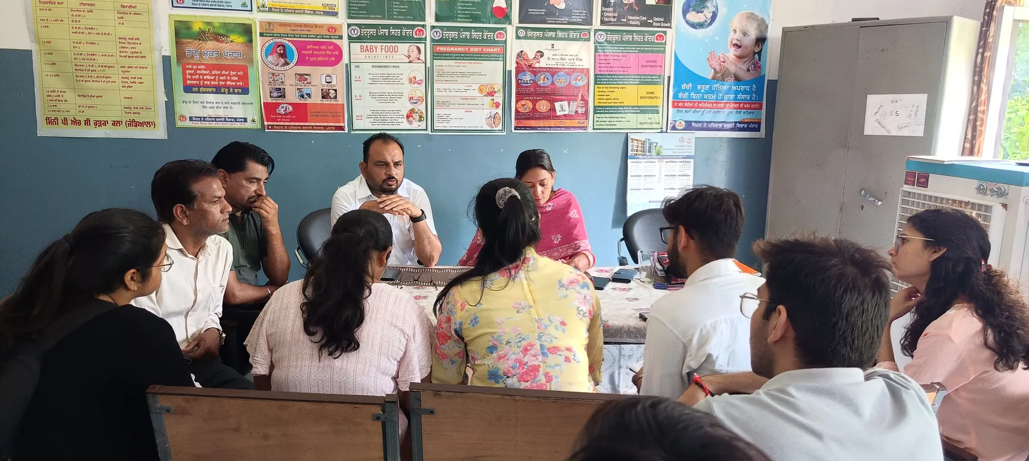 Participants seated around a table in discussion, with educational posters on the wall behind them.